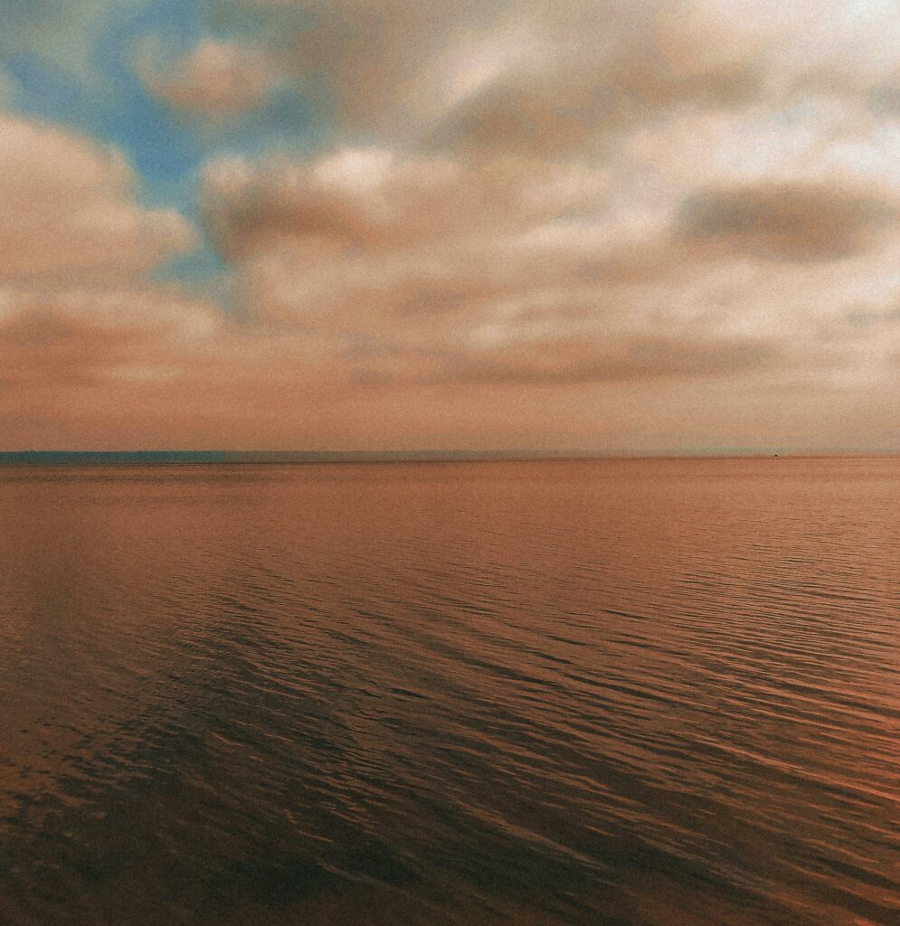 Calm ocean with a cloudy sky and warm hues, creating a tranquil sunset atmosphere.